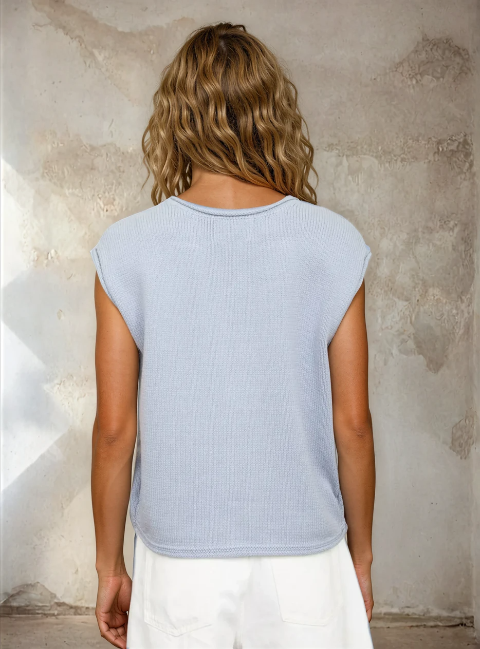 Person wearing a light blue sleeveless top against a textured wall.