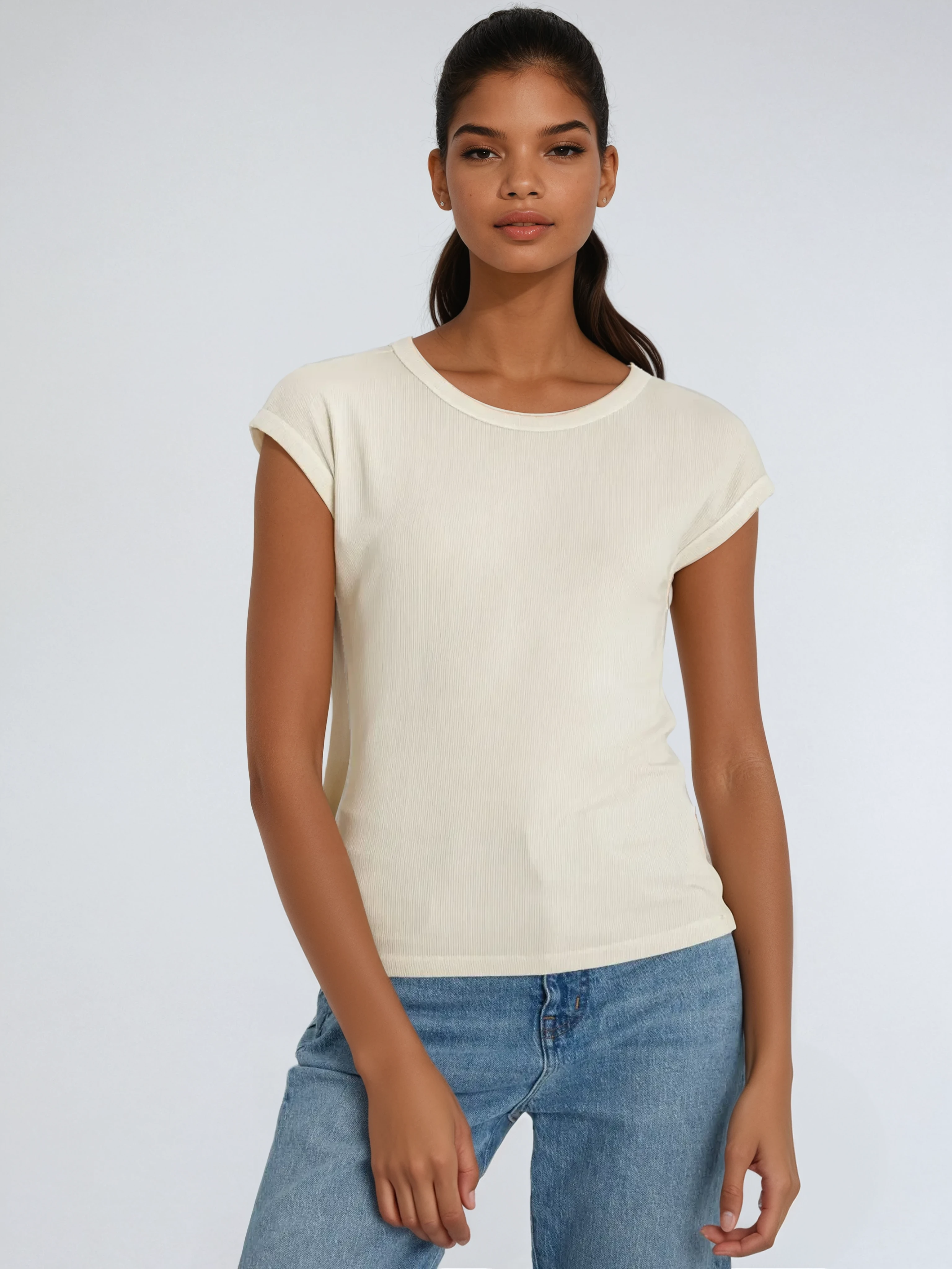 Woman wearing a beige top and blue jeans against a plain background