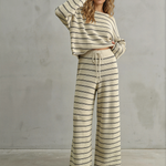 Woman wearing a striped outfit against a gray concrete wall.