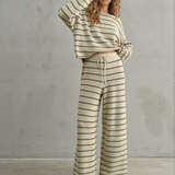 Woman wearing a striped outfit against a gray concrete wall.