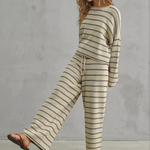 Woman wearing a striped sweater and pants set against a gray concrete wall.