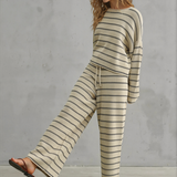 Woman wearing a striped sweater and pants set against a gray concrete wall.