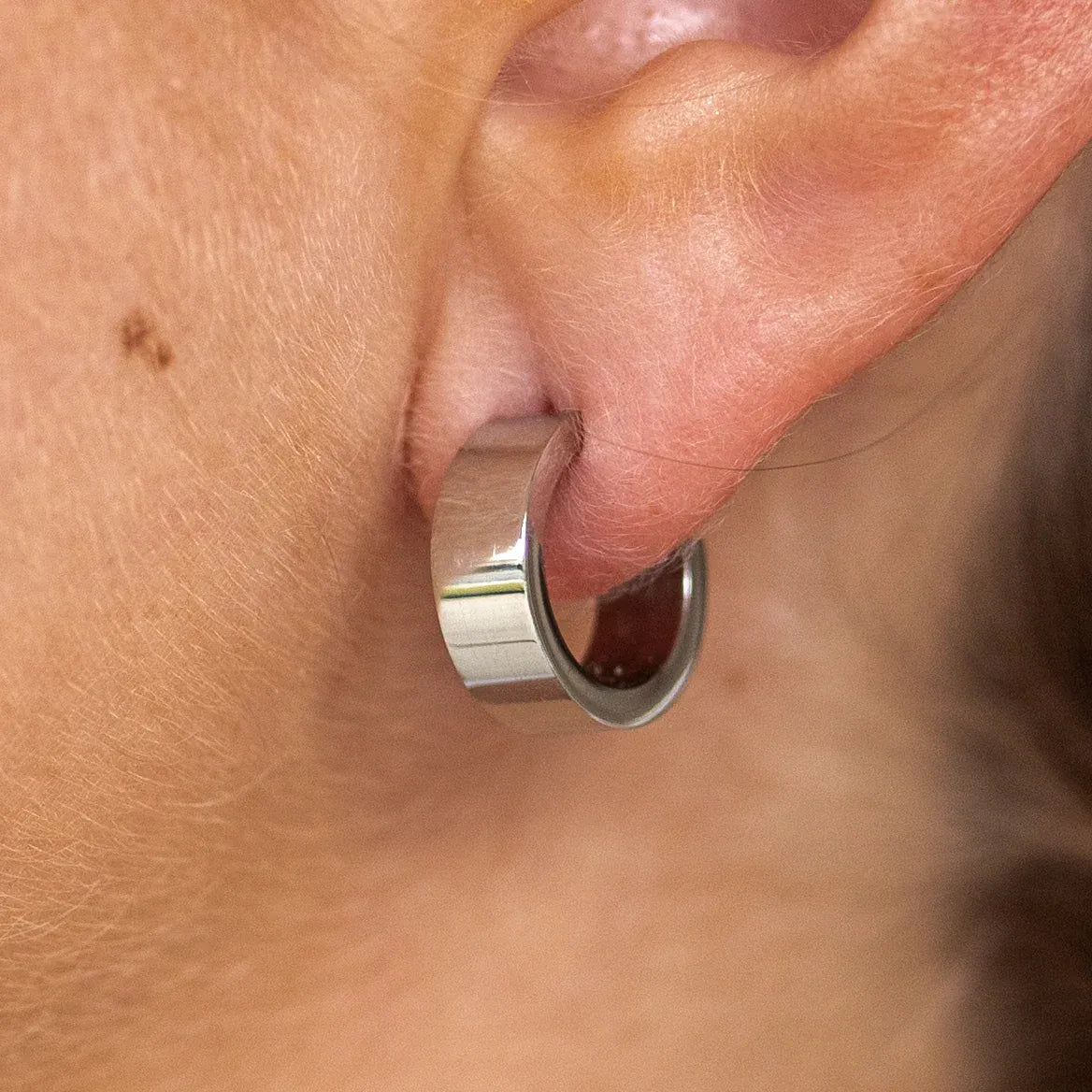 A close-up image of a silver-colored hoop earring on an ear.