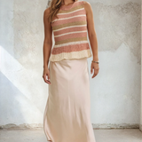 Woman wearing a striped sleeveless top and beige skirt against a textured wall.