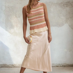 Woman wearing a striped top and satin skirt against a textured wall.