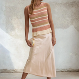Woman wearing a striped top and satin skirt against a textured wall.