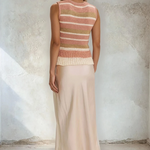 Woman wearing a sleeveless striped top and long skirt against a textured wall.