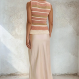 Woman wearing a sleeveless striped top and long skirt against a textured wall.