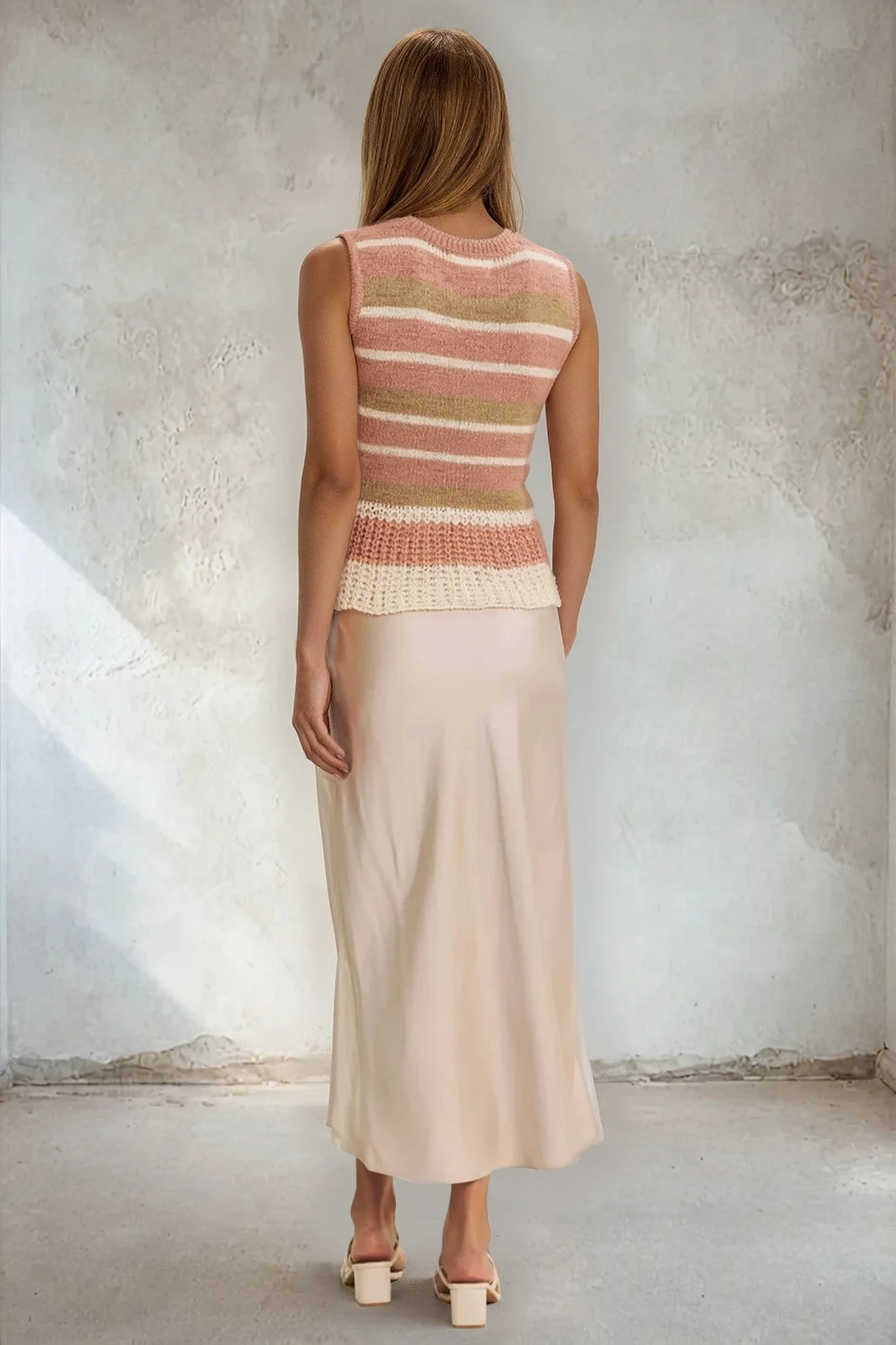 Woman wearing a sleeveless striped top and long skirt against a textured wall.