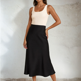 Woman wearing a two-tone dress with a white top and black skirt against a plain background
