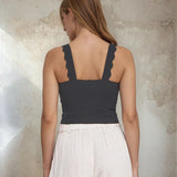Woman wearing a dark gray tank top with lace trim against a textured wall.