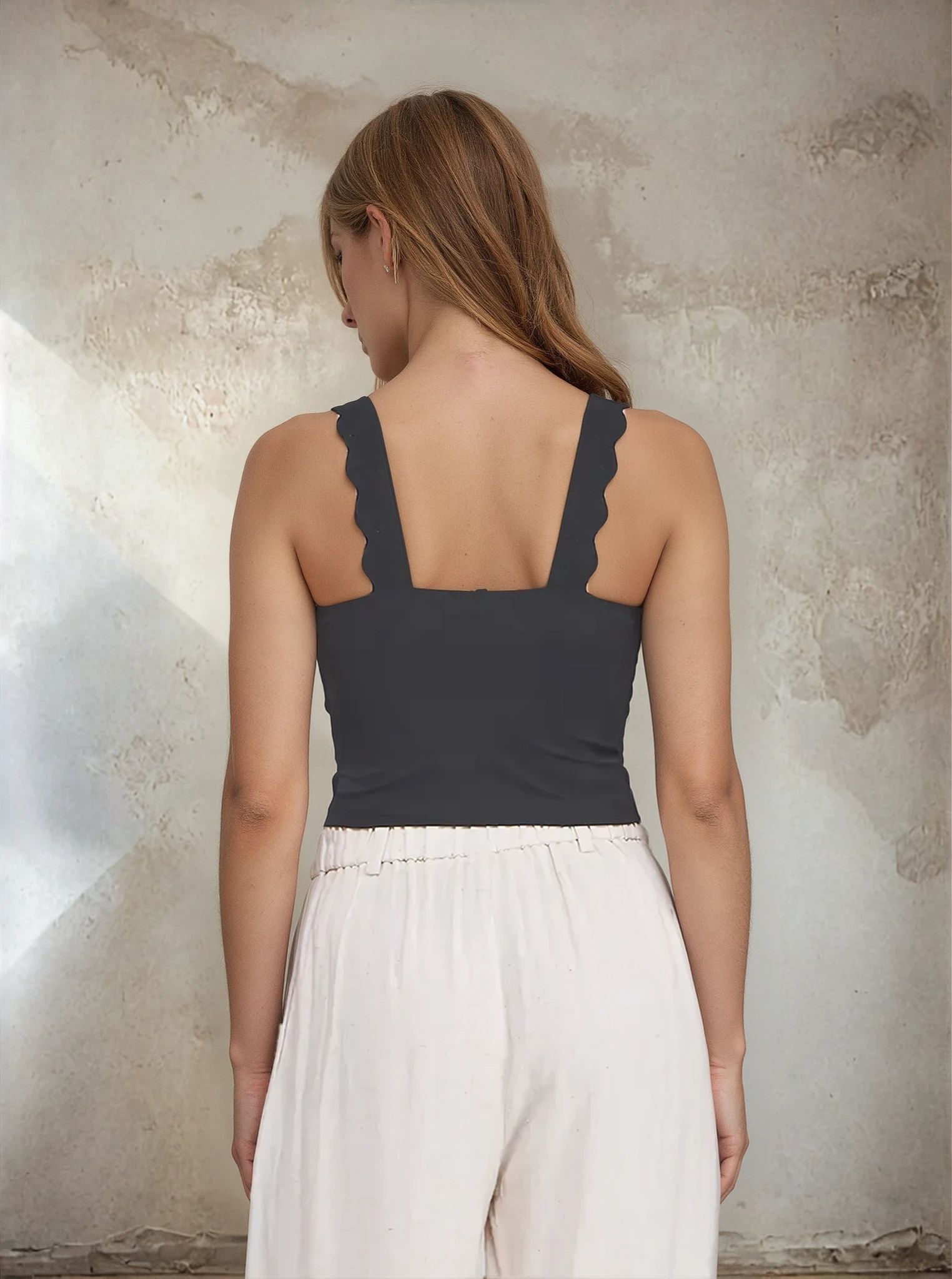 Woman wearing a dark gray tank top with lace trim against a textured wall.