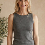 Woman in gray sleeveless top and shorts holding a woven bag indoors with a plant in the background.