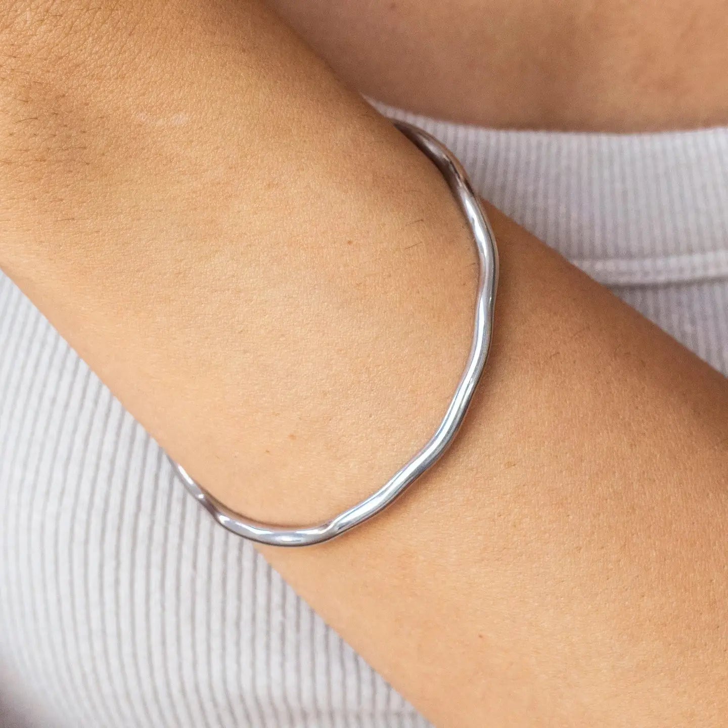 Silver bangle on a person's wrist with a neutral background