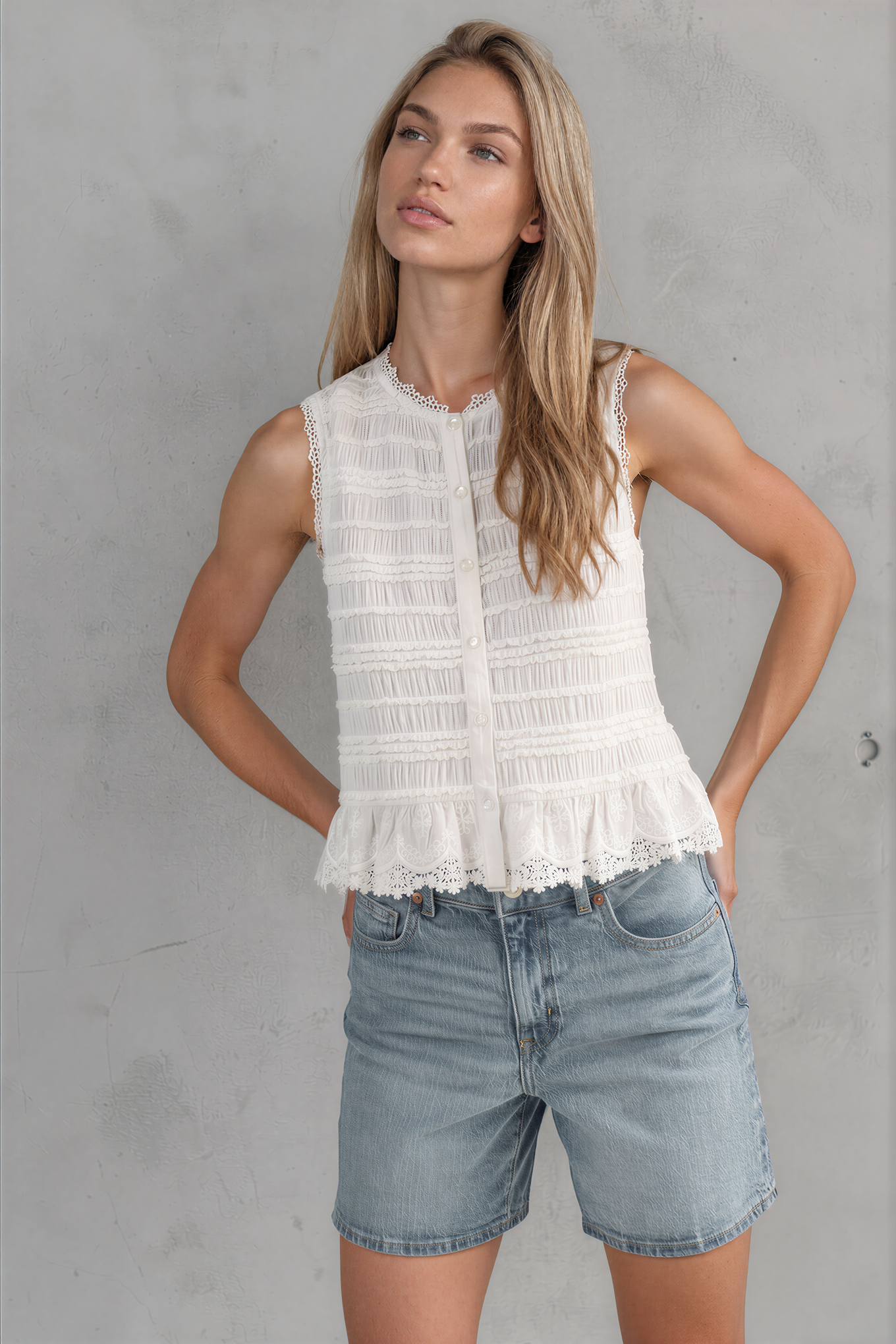 Woman wearing a white sleeveless top and denim shorts against a gray background