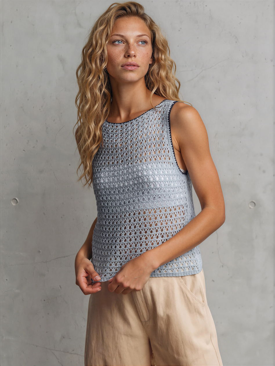 Woman wearing a sleeveless crochet top against a concrete wall.