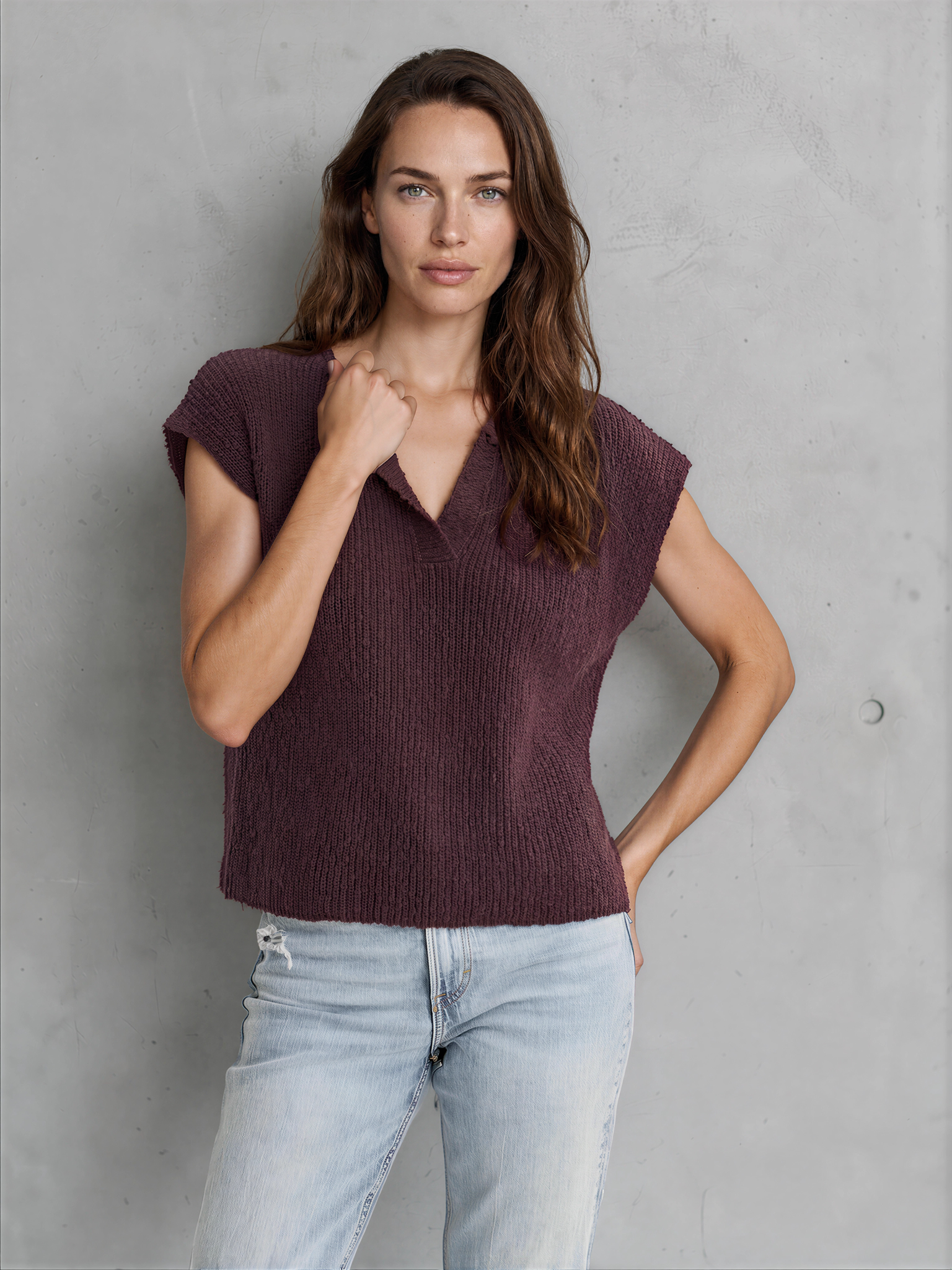 Woman wearing a maroon sleeveless top and light blue jeans against a gray background