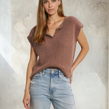 Woman wearing a brown knit top and light blue jeans against a textured wall.