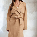 Woman wearing a beige trench coat against a textured white background
