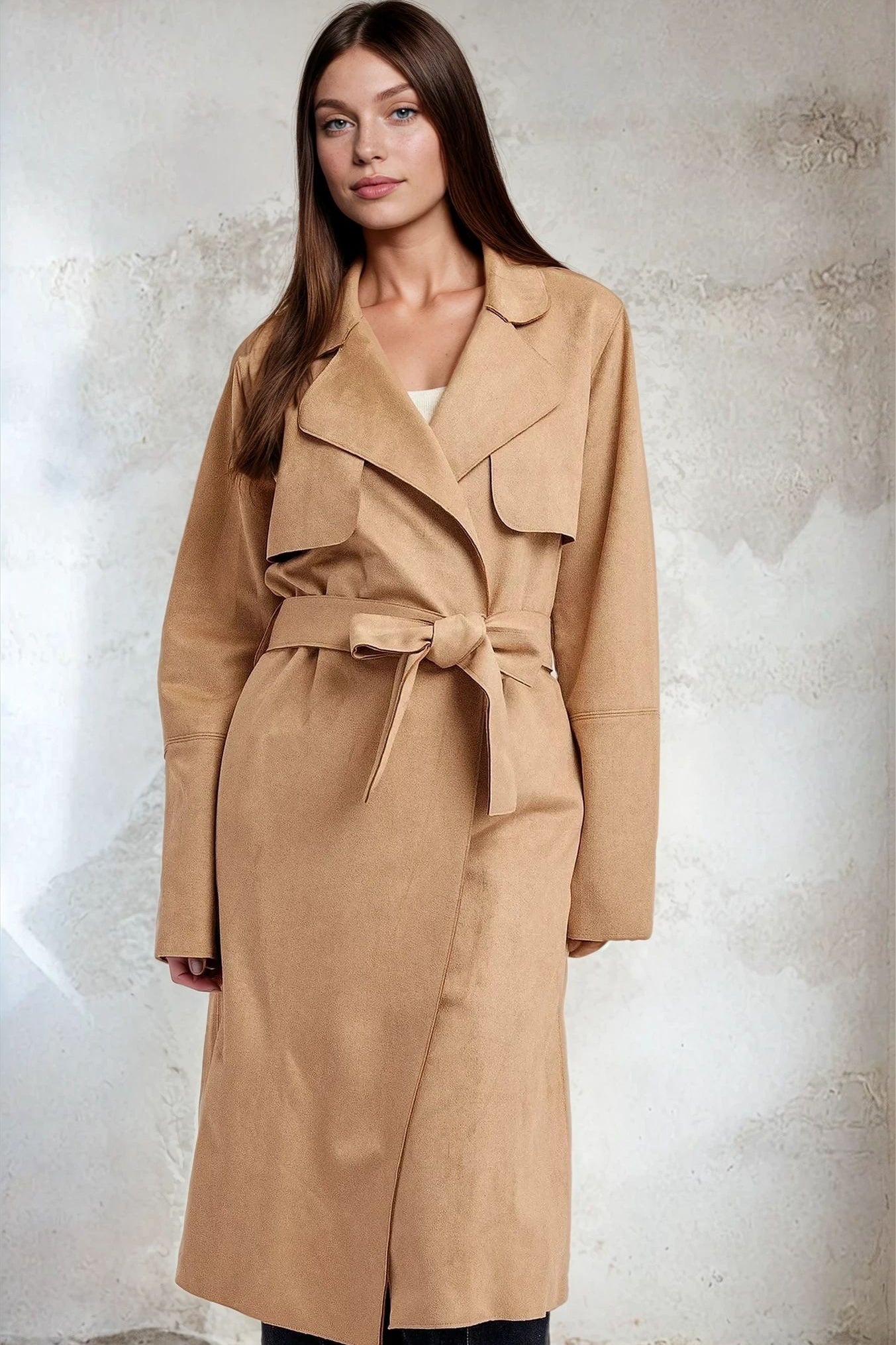 Woman wearing a beige trench coat against a textured white background