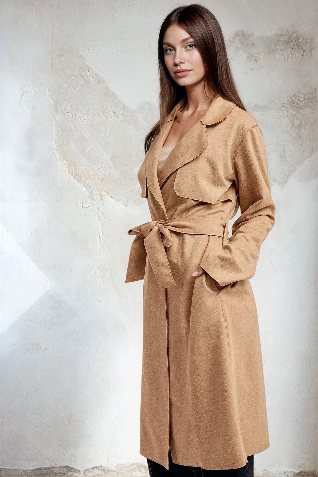 Woman wearing a beige trench coat against a textured white wall
