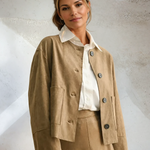 Woman wearing a beige suit with a white shirt against a textured wall.