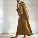 Woman wearing a beige suit standing against a white wall.