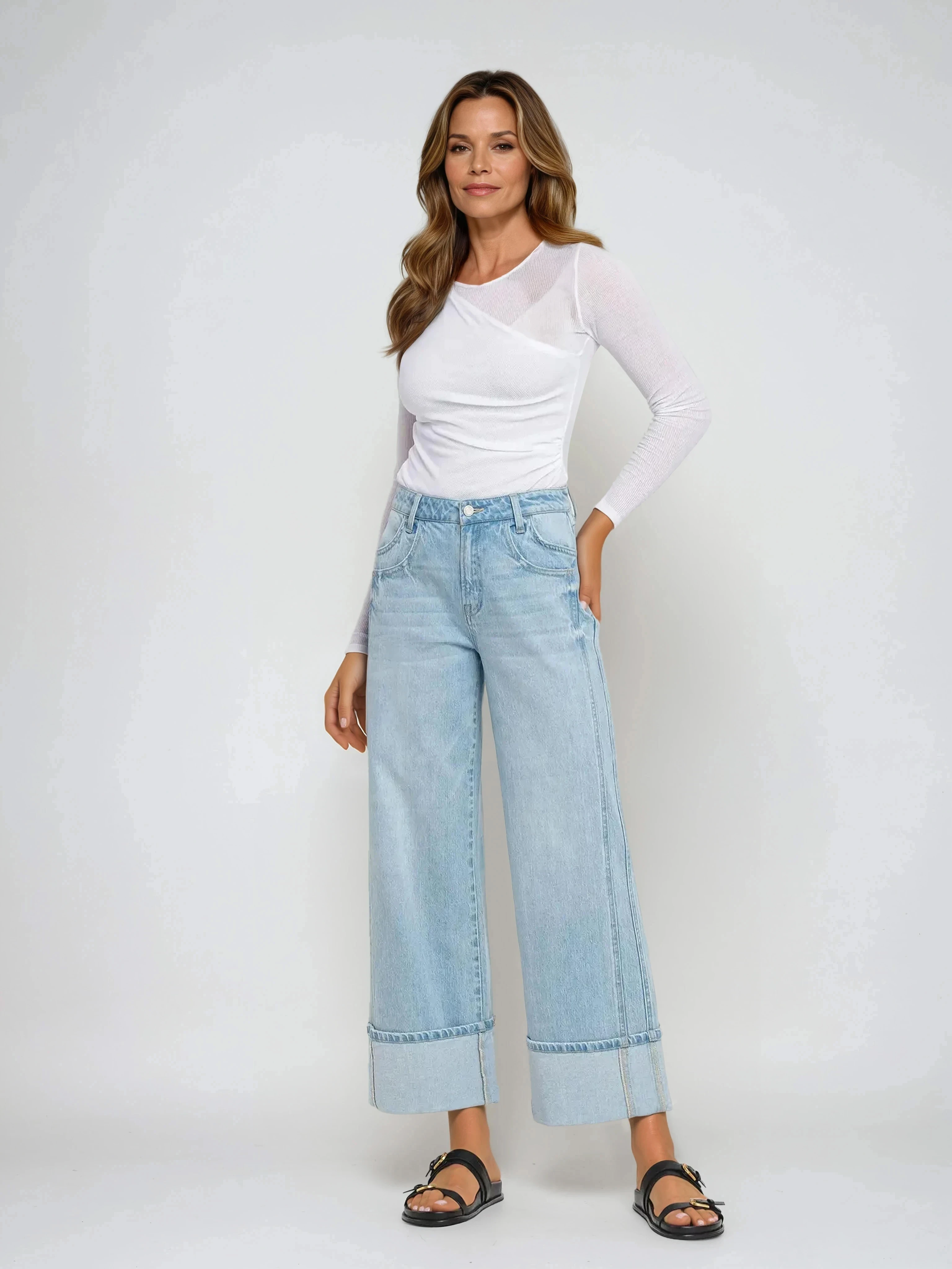 Woman wearing a white long-sleeve top and light blue jeans on a white background