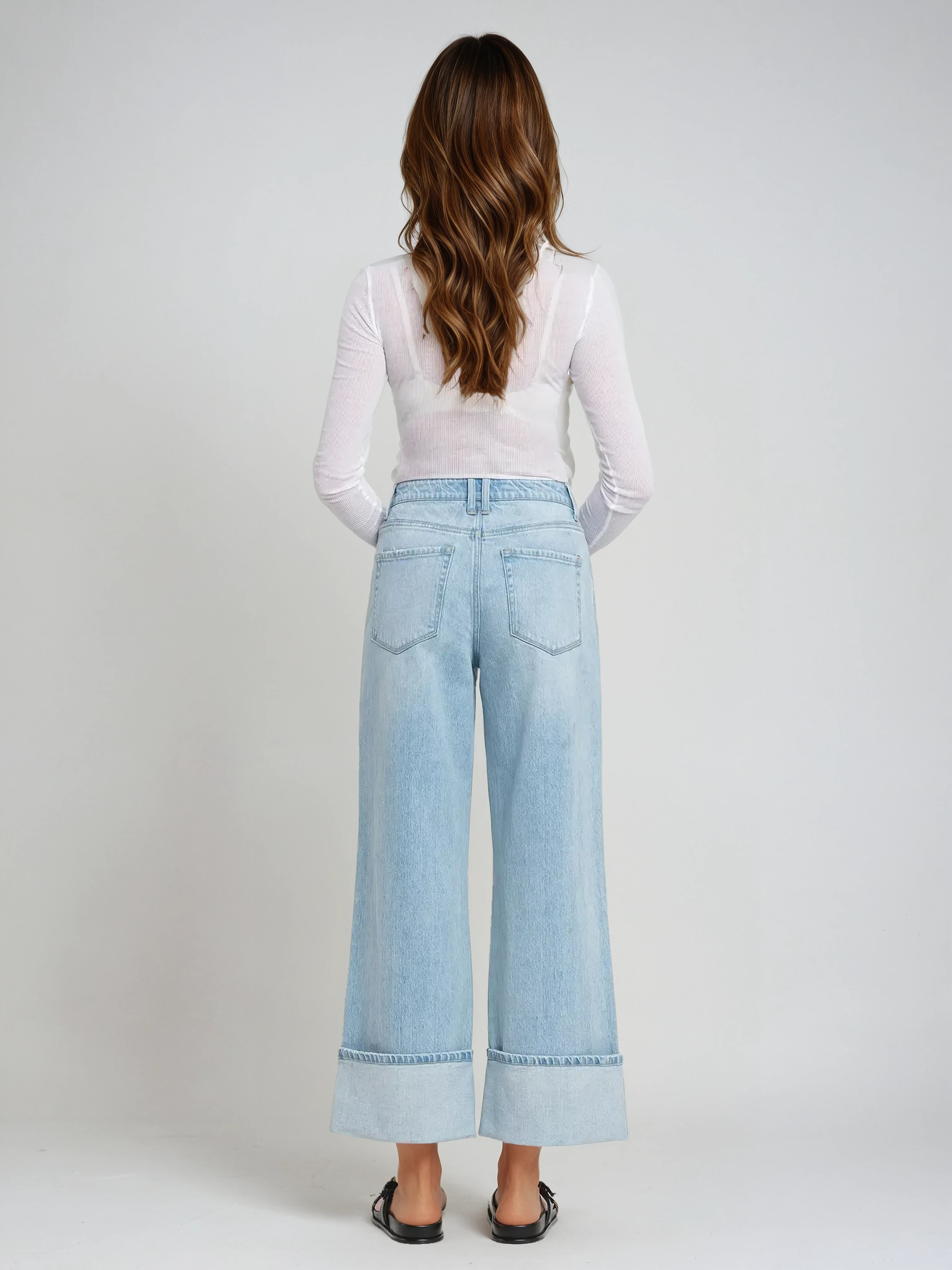 Woman wearing light blue wide-leg jeans and a white top on a plain background
