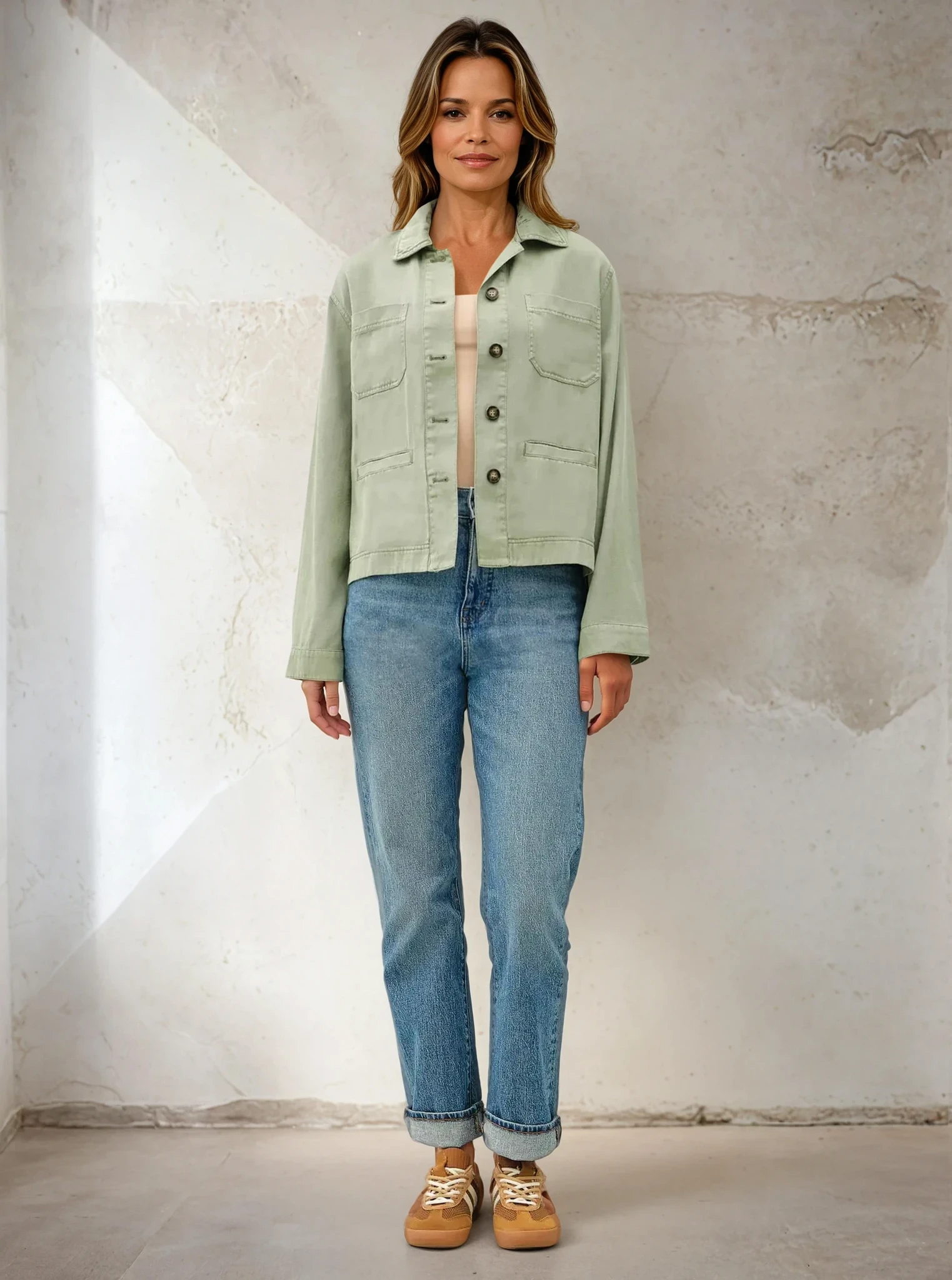 Woman wearing a light green jacket and blue jeans against a textured wall.