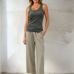 Woman wearing a green tank top and beige pants against a plain background