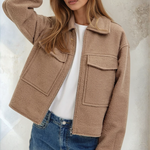 Woman wearing a beige jacket and blue jeans against a neutral background