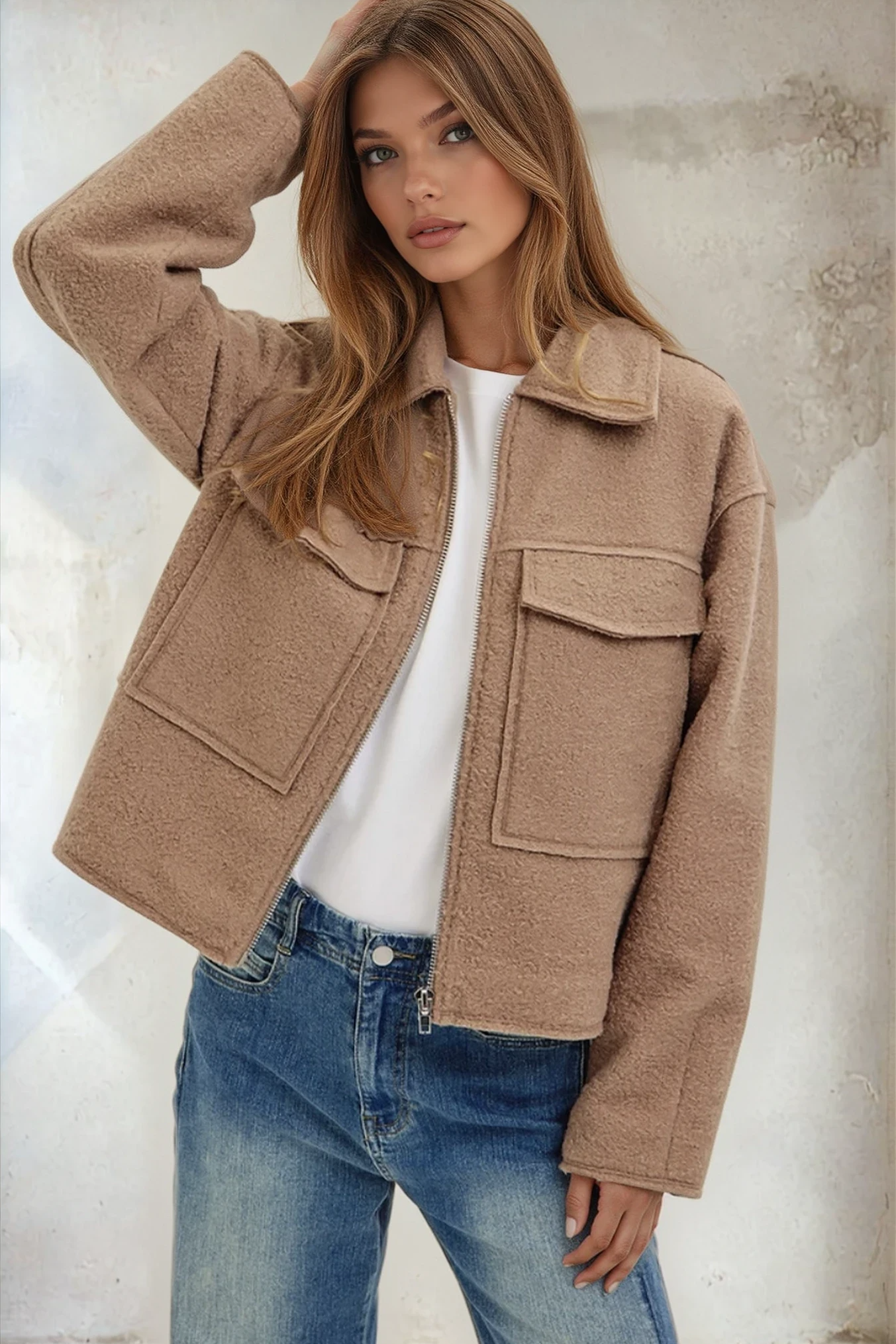Woman wearing a beige jacket and blue jeans against a neutral background