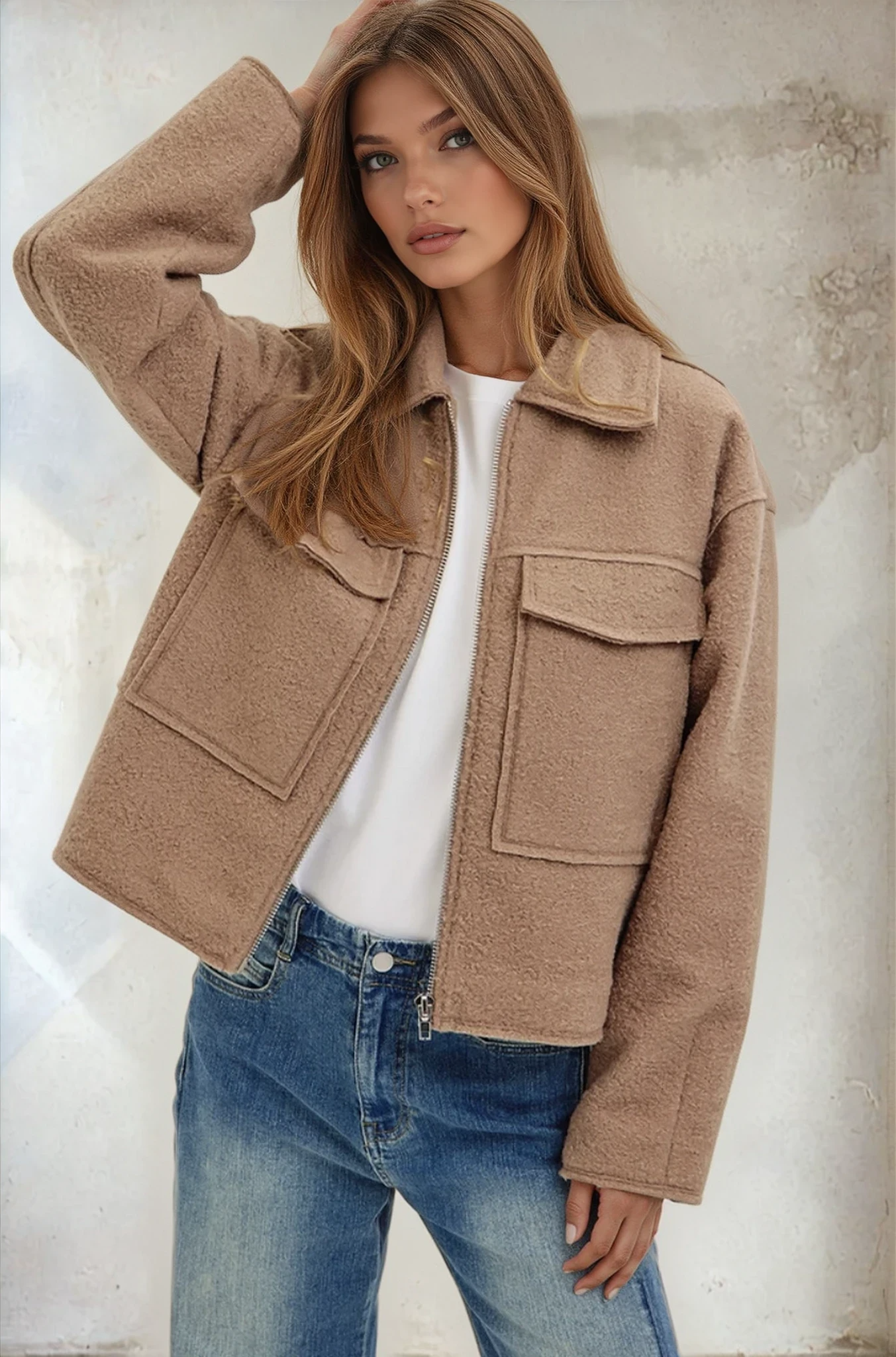 Woman wearing a beige jacket and blue jeans against a neutral background