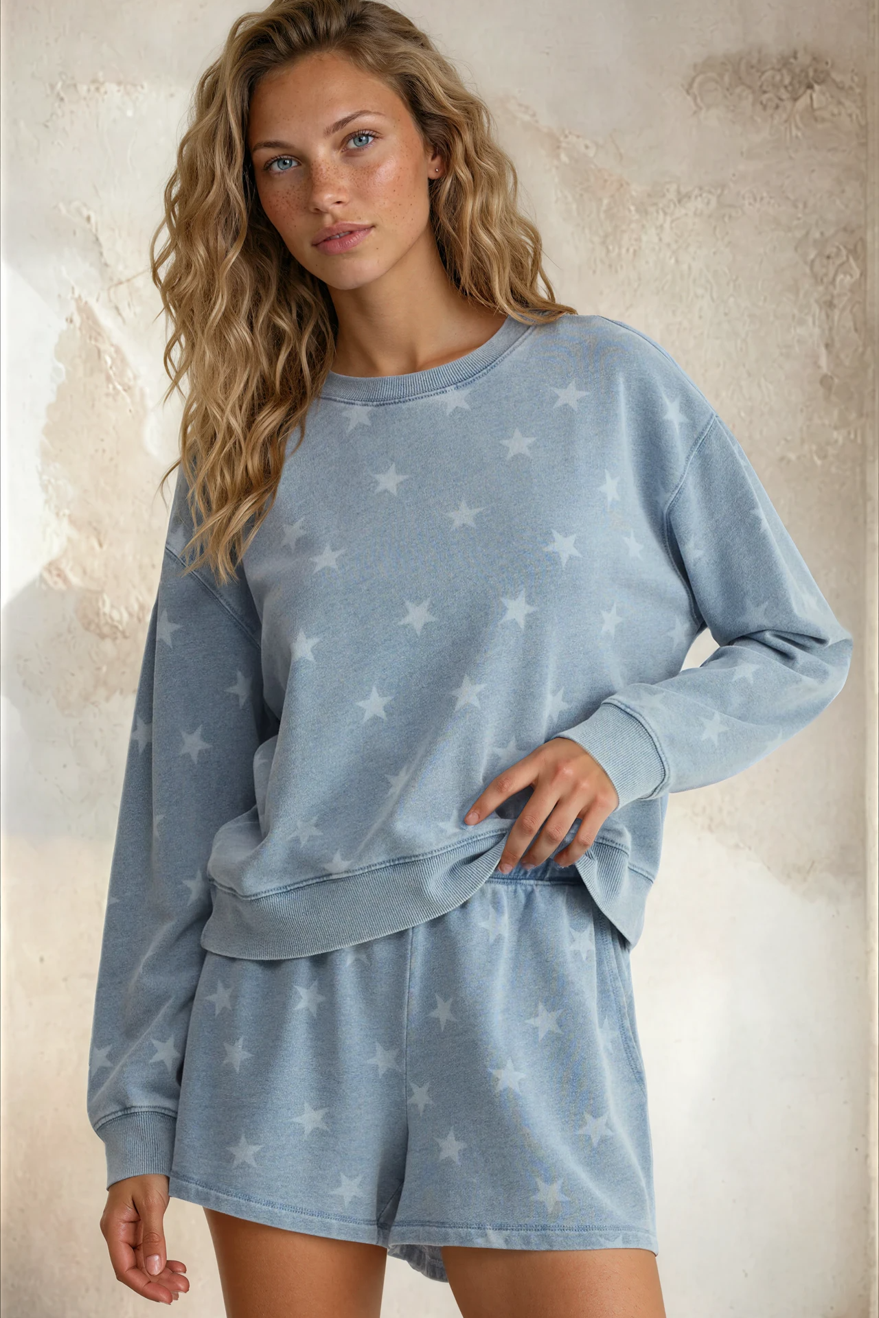 Woman wearing a blue star-patterned loungewear set against a textured wall.