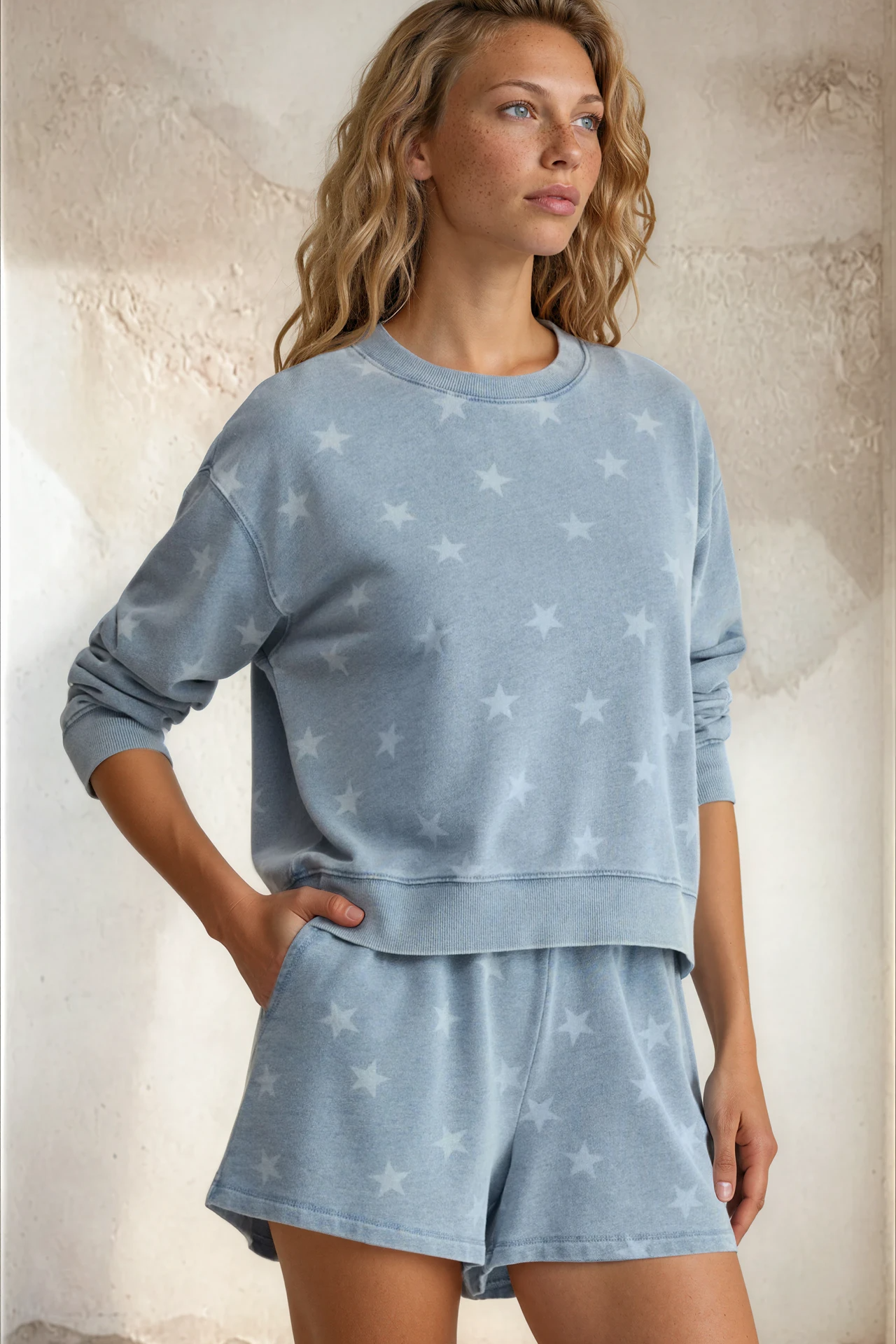 Woman wearing a light blue pajama set with star patterns against a textured wall.