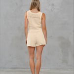 Woman wearing a beige sleeveless top and shorts set against a gray background