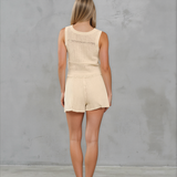 Woman wearing a beige sleeveless top and shorts set against a gray background