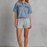 Woman wearing a denim shirt and shorts against a gray background