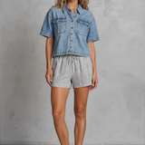 Woman wearing a denim shirt and shorts against a gray background