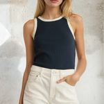 Woman wearing a black tank top with white trim and white shorts against a textured wall.