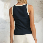 Woman wearing a navy tank top with white trim and white shorts against a textured wall.