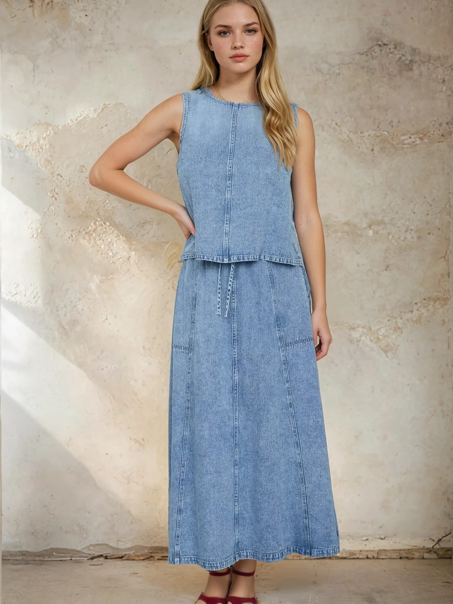 Woman wearing a denim dress against a textured wall.