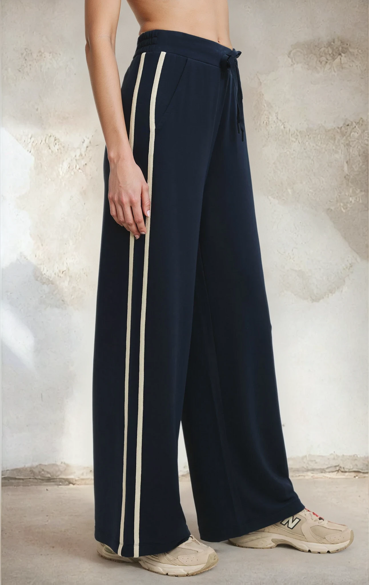 Navy wide-leg pants with white stripes worn by a person against a textured wall.