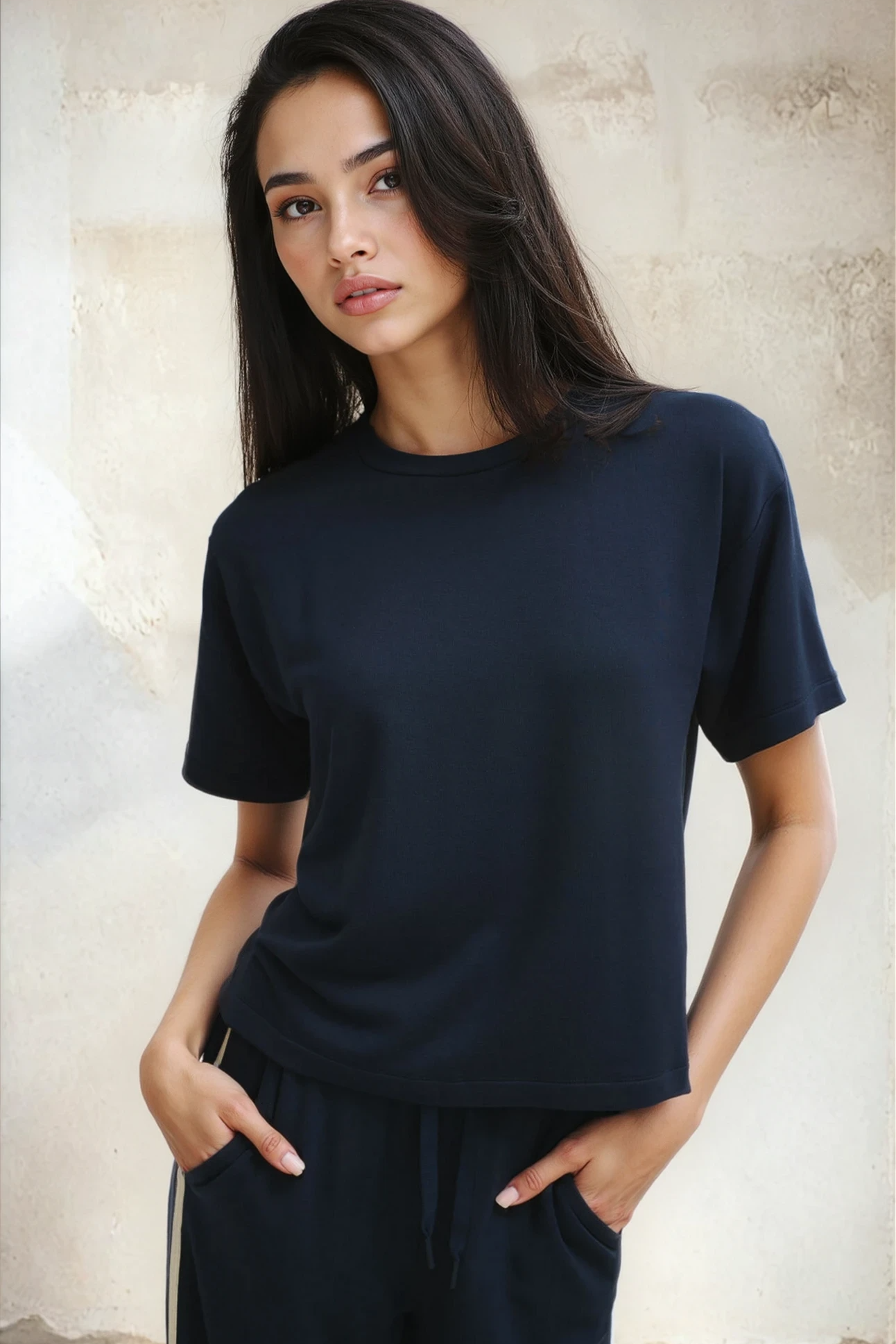 Woman wearing a black t-shirt and dark pants against a neutral background