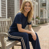 Woman sitting on a bench in a quaint town setting wearing a navy tracksuit.