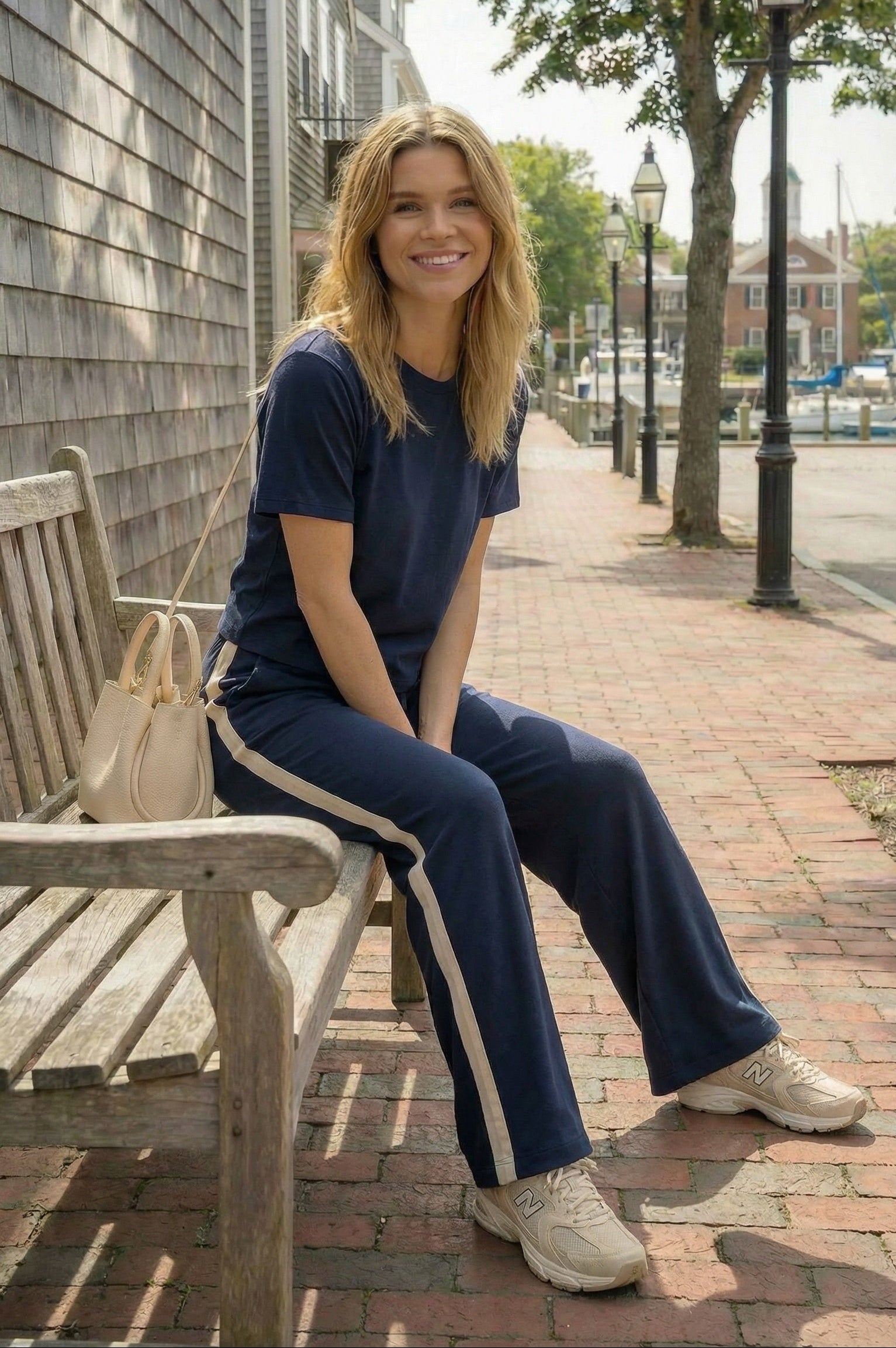 Woman sitting on a bench wearing a navy outfit with white stripes in an urban setting.