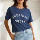 Woman wearing a blue 'American Grown' t-shirt and denim shorts against a neutral background