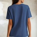 Woman wearing a blue t-shirt and light denim shorts against a textured wall.