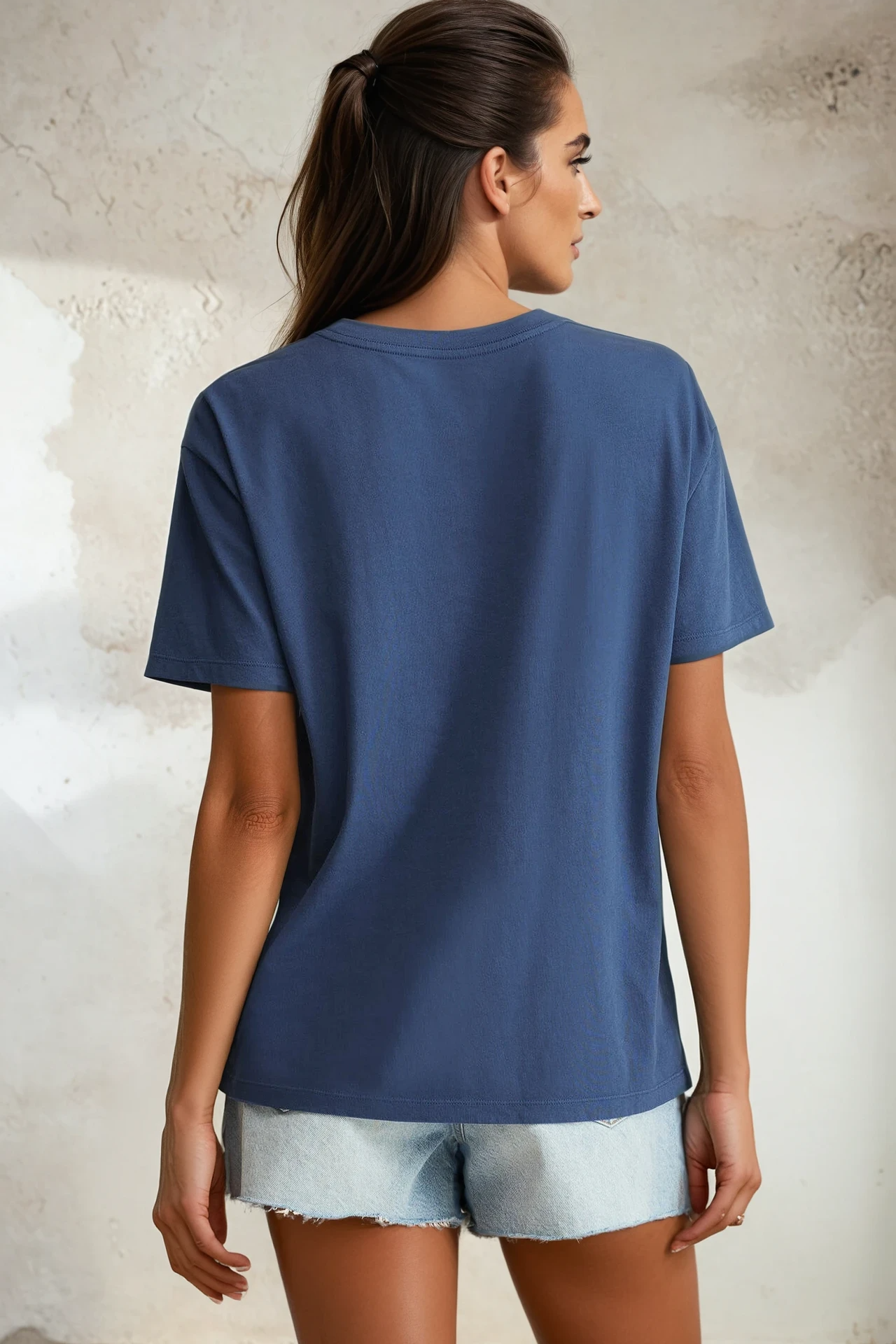 Woman wearing a blue t-shirt and light denim shorts against a textured wall.